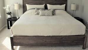 A large bed with a dark headboard, two bedside tables with lamps, and a potted plant on one side. - Stylish modern home- explore PNW Hike work from home or explore nearby wineries  (Battle Ground)