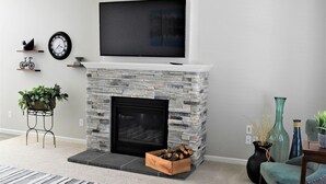 A living room with a stone fireplace, a mounted TV, and decorative items. - Stylish modern home- explore PNW Hike work from home or explore nearby wineries  (Battle Ground)
