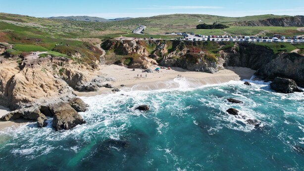 A coastal landscape with a beach, rocky cliffs, and a parking area. - Bodega Bay - Sonoma Coastline (Bodega Bay)
