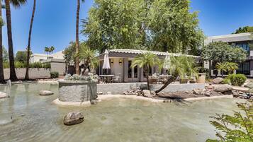 A serene outdoor area with a pool, palm trees, and a small building with outdoor seating.