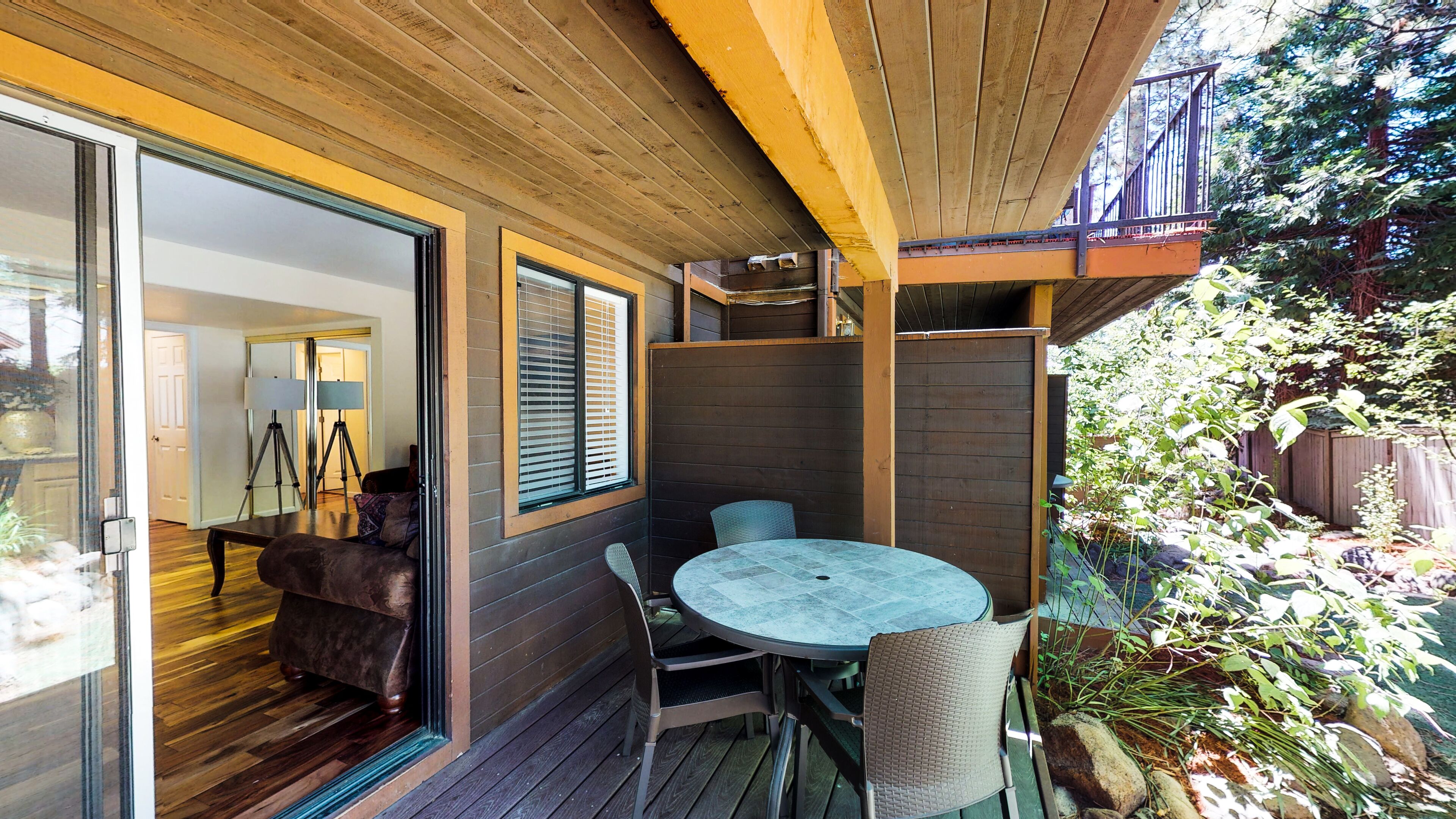 An outdoor patio with a round table and chairs, wooden deck flooring, and a view of the backyard.