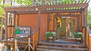 A wooden lodge entrance with a sign for North Lake Lodges & Villas, featuring a porch and steps leading to the door.
