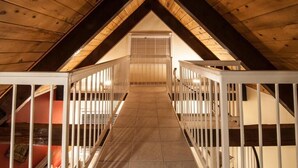An attic room with a sloped ceiling, wooden beams, and a central staircase with white railings.