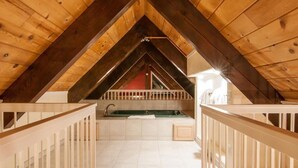 An attic bedroom with a sloped ceiling, a built-in bathtub, and a white railing around the window.