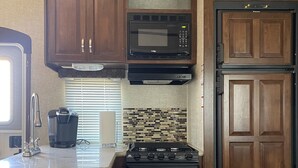 Une cuisine compacte avec des meubles en bois, un four à micro-ondes, une cuisinière et une machine à café.