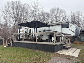 A recreational vehicle with a covered deck area and outdoor seating.