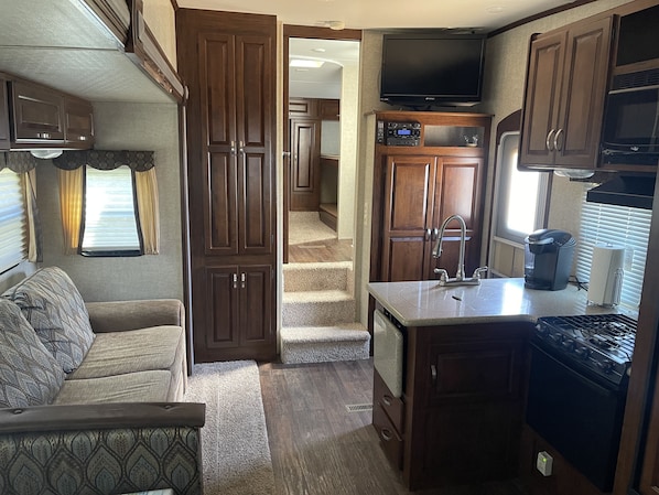 A compact RV kitchen with wooden cabinets, a built-in stove, and a television above the counter.