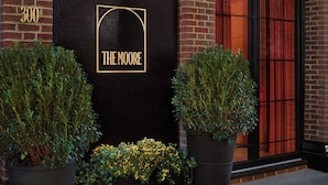 A black door with "THE MOORE" in gold lettering, flanked by two potted plants, and a brick building facade. - The Moore, a Member of Design Hotels (New York)