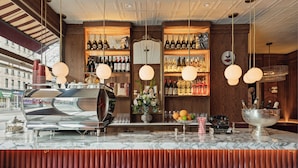 A bar area with a marble countertop, multiple wine bottles, a coffee machine, and bar stools. - The Moore, a Member of Design Hotels (New York)