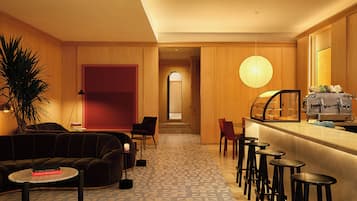 A modern hotel lobby with a sofa, chairs, a bar area, and a large plant.