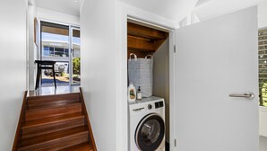 A modern laundry room with a washing machine, a wooden staircase, and a view of a patio area. - Rock Ledge - Woolgoogla Headland (Woolgoolga)