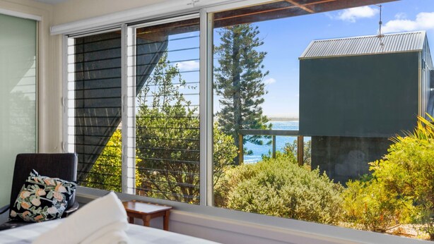 A bedroom with a large window overlooking a garden and a building with a metal roof. - Rock Ledge - Woolgoogla Headland (Woolgoolga)