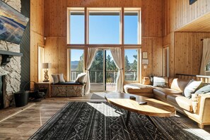 Un salon spacieux avec une cheminée en pierre, une grande fenêtre avec des rideaux, une table basse en bois et un canapé beige.