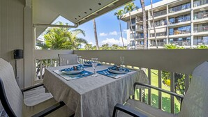 A balcony with a table set for two, overlooking a building with multiple balconies and palm trees. - *25% Off-Steps to Beach-AC in Every Room-Remodeled (Kihei)