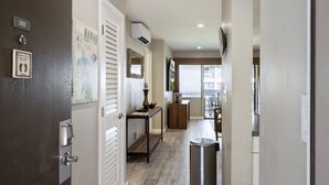 A hallway with a door labeled 202, a small table with a lamp, a trash bin, and a view of a dining area. - *25% Off-Steps to Beach-AC in Every Room-Remodeled (Kihei)