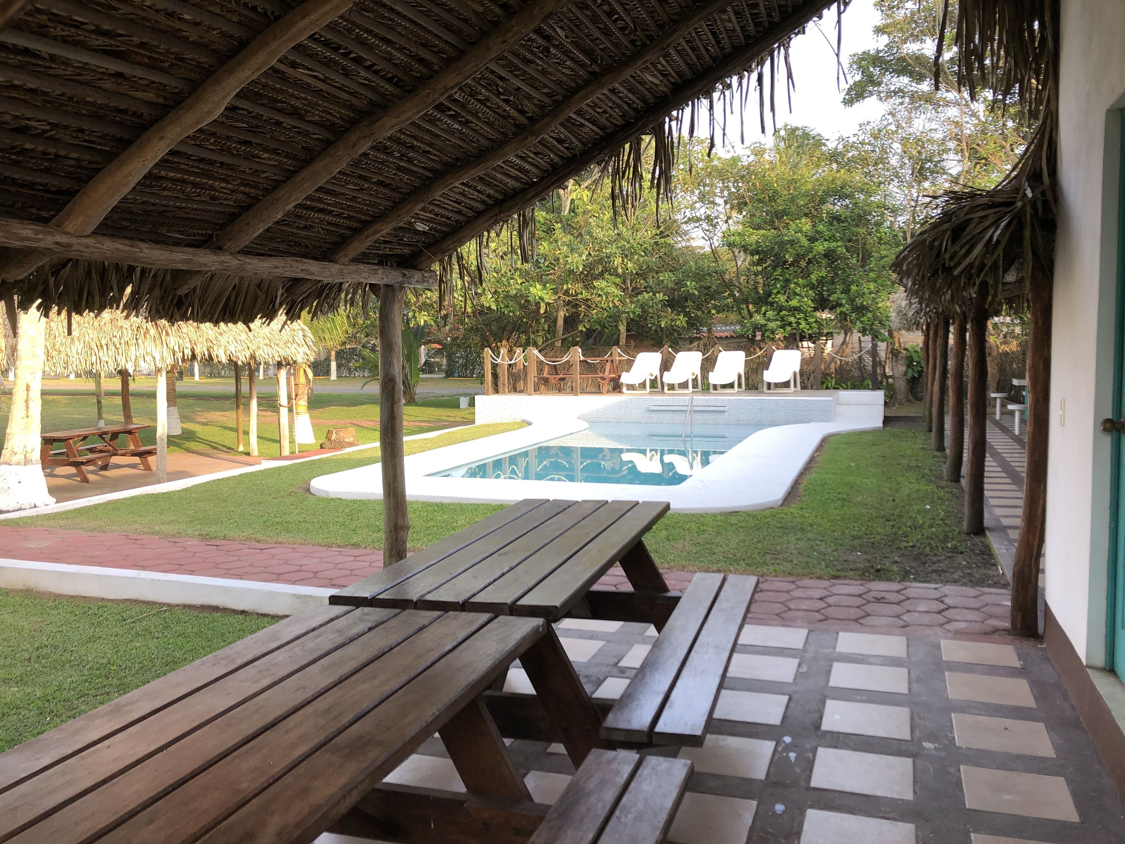 Un espacio al aire libre techado con piscina, mesas de picnic y sillas de descanso.