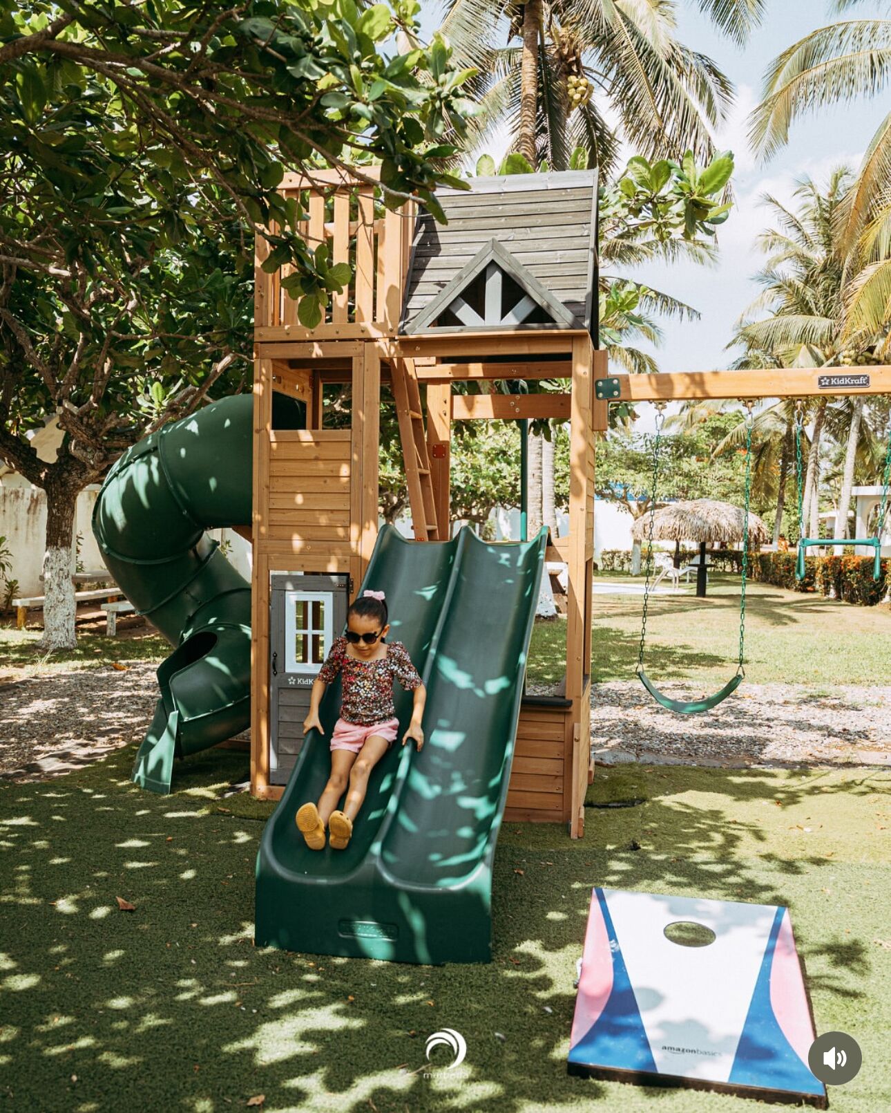A wooden play structure with a slide and a swing set in a park.