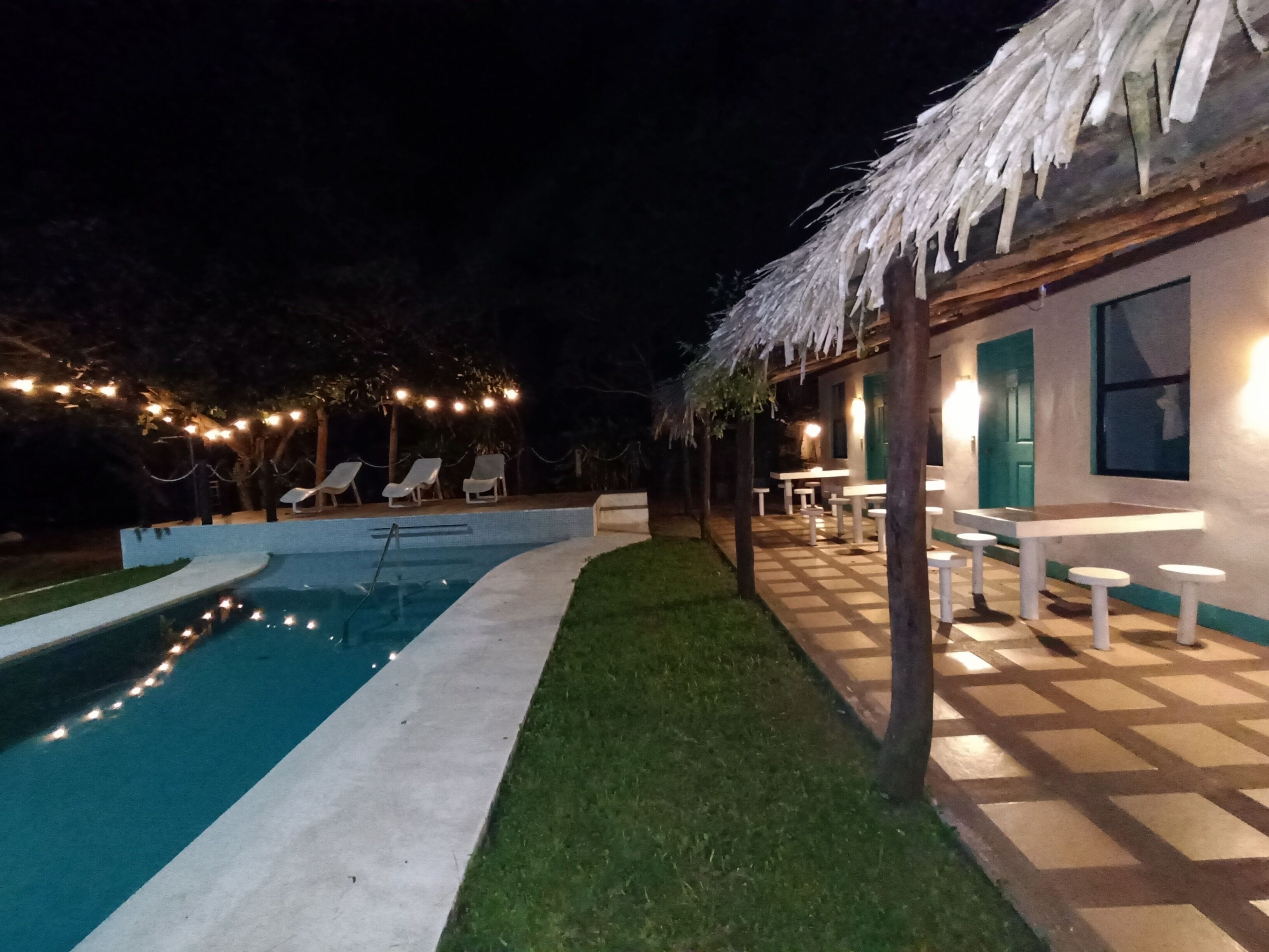 A pool area with lounge chairs and a thatched-roof building.