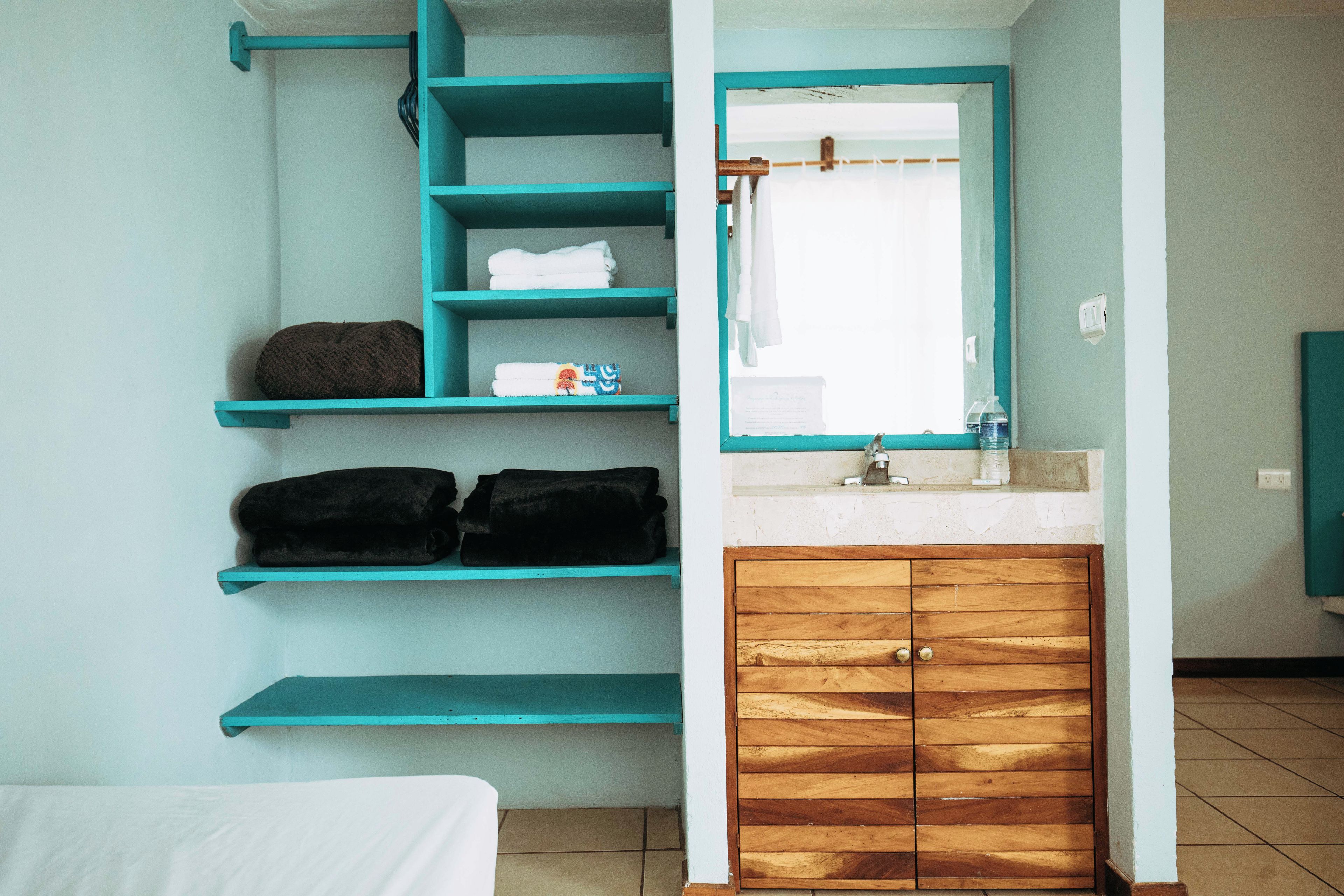 A bathroom with teal shelves, a wooden cabinet, and a mirror.