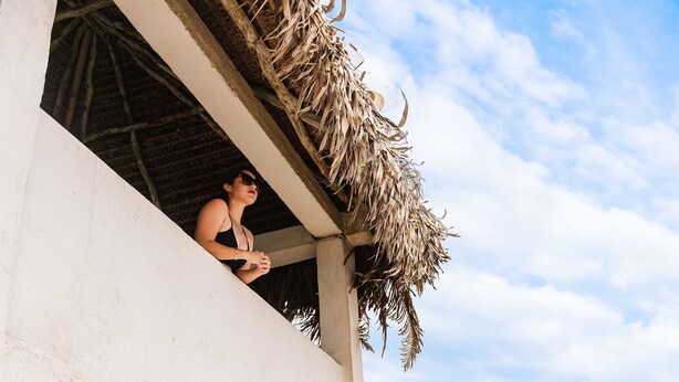 A beachside hotel with a balcony overlooking the ocean, thatched umbrellas, and lounge chairs.