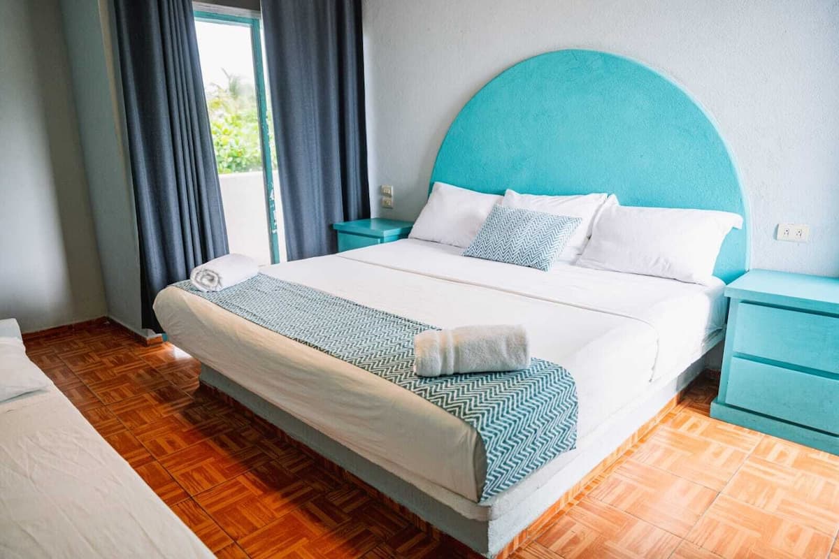 A neatly made bed with a patterned bedspread and pillows, a teal headboard, and a wooden floor.