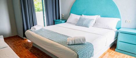 A neatly made bed with a patterned bedspread and pillows, a teal headboard, and a wooden floor.