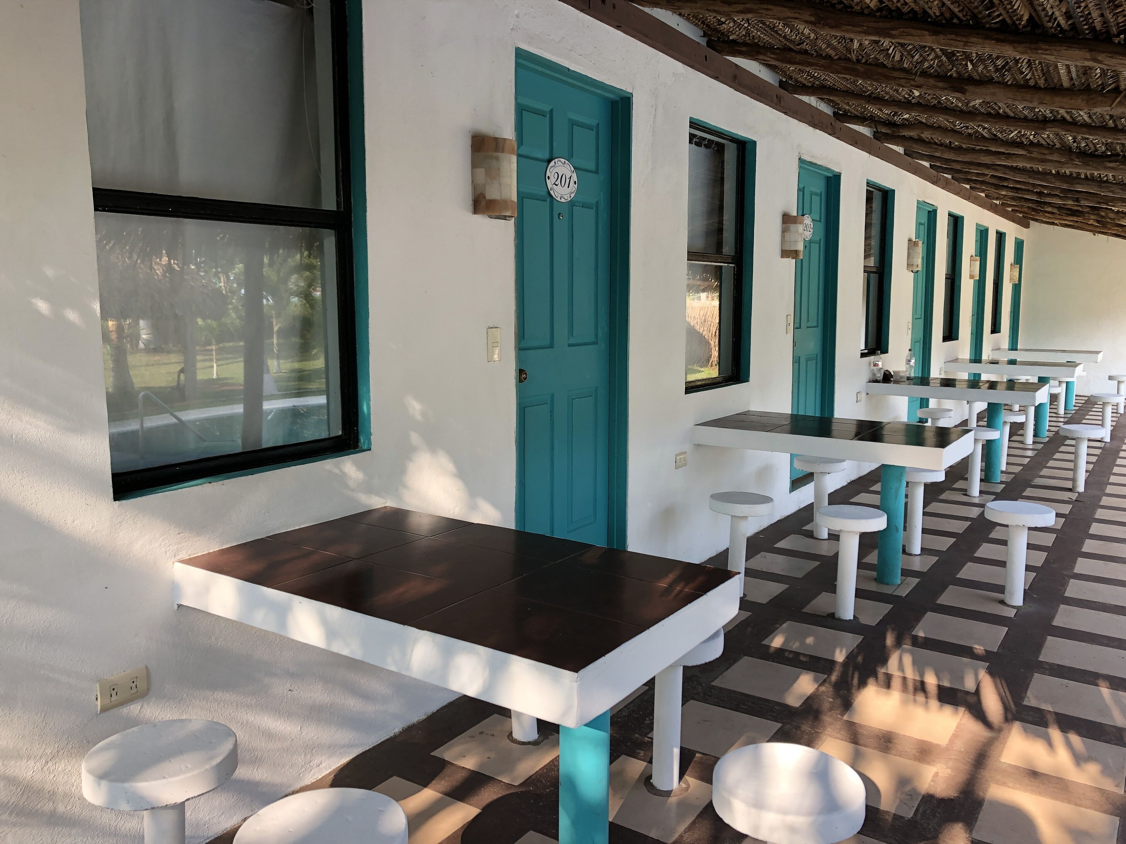 A row of tables and chairs in a covered outdoor area with a checkered floor pattern.