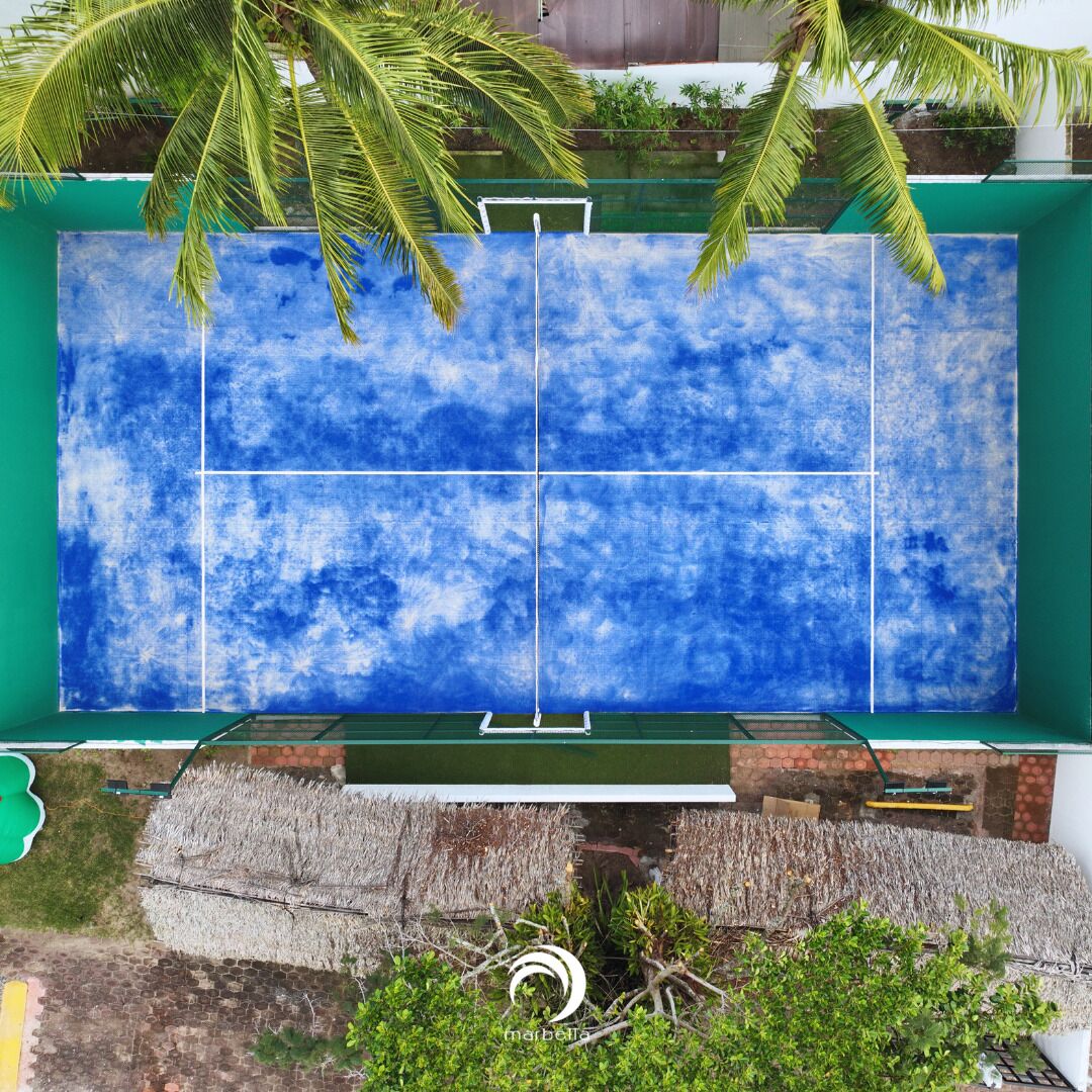 Una amplia piscina azul con baldosas y fondo de cristal, rodeada de vegetación y un muro de ladrillo.