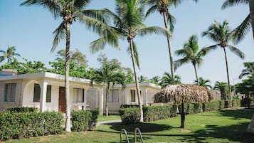 A resort with palm trees, a pool, and a thatched-roof structure.