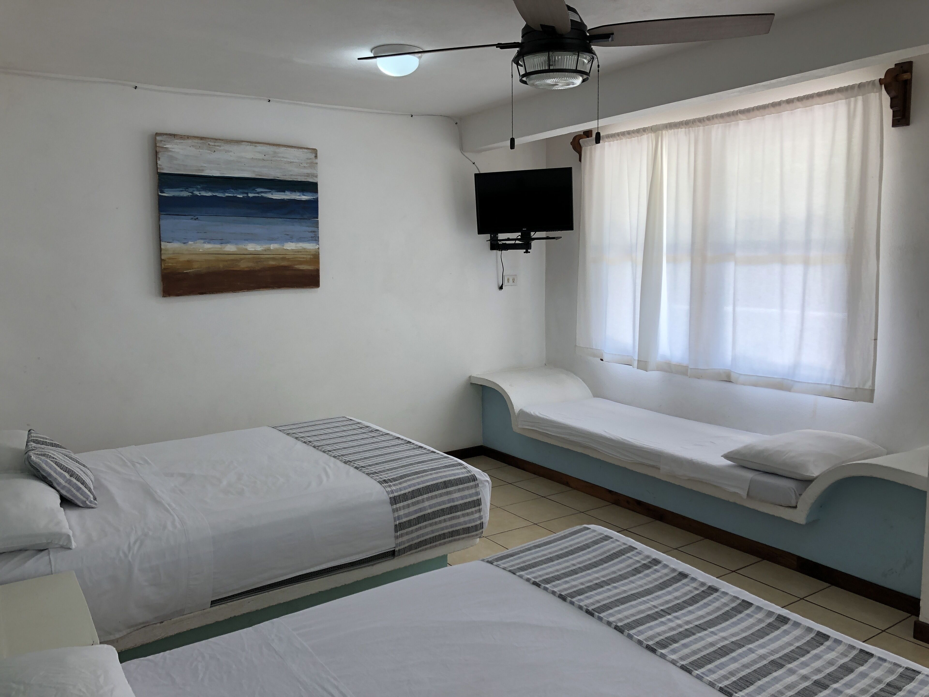 A room with two beds, a ceiling fan, a TV, and a window with curtains.