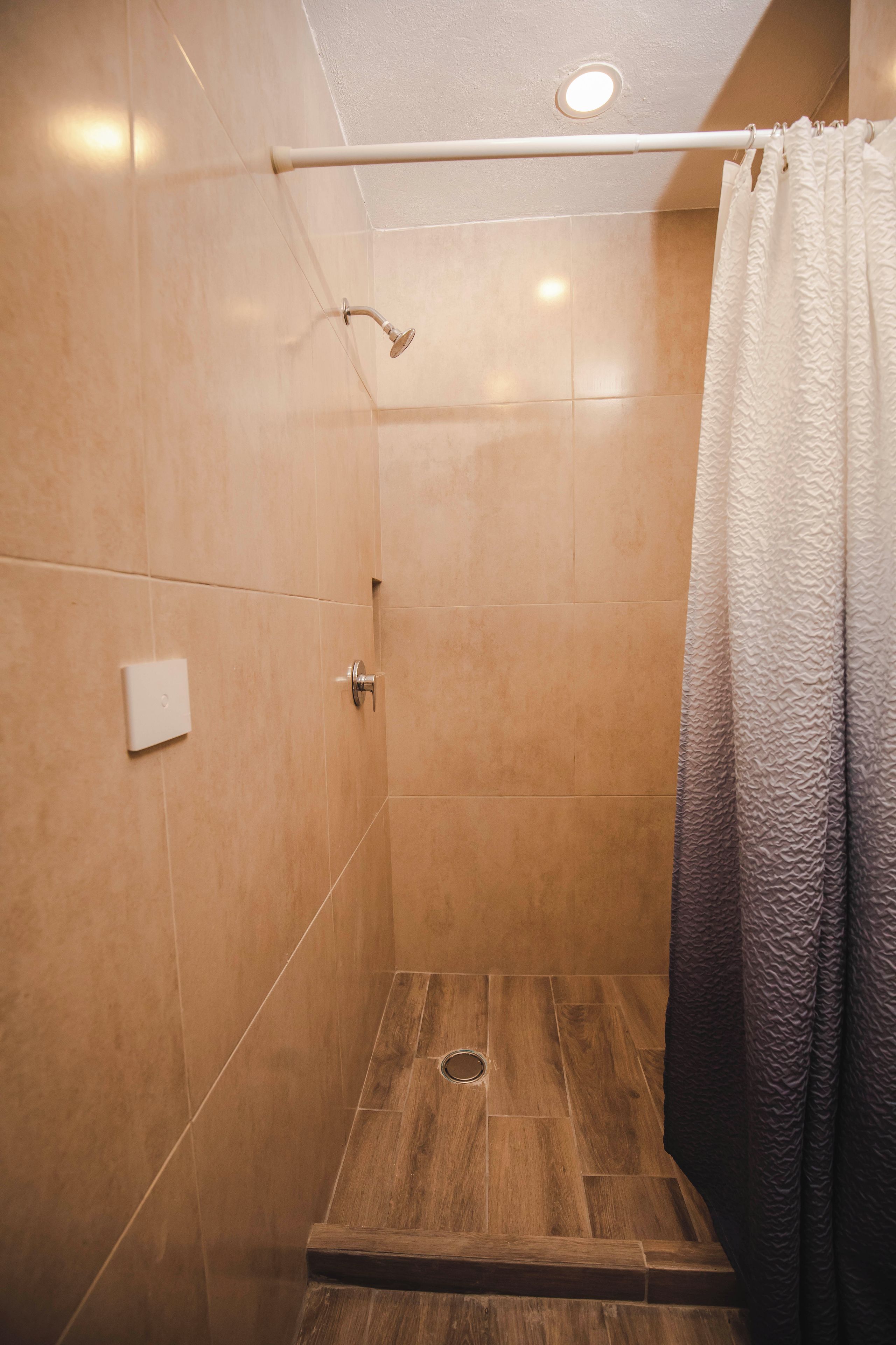 A shower area with a wooden floor, a showerhead, and a curtain.