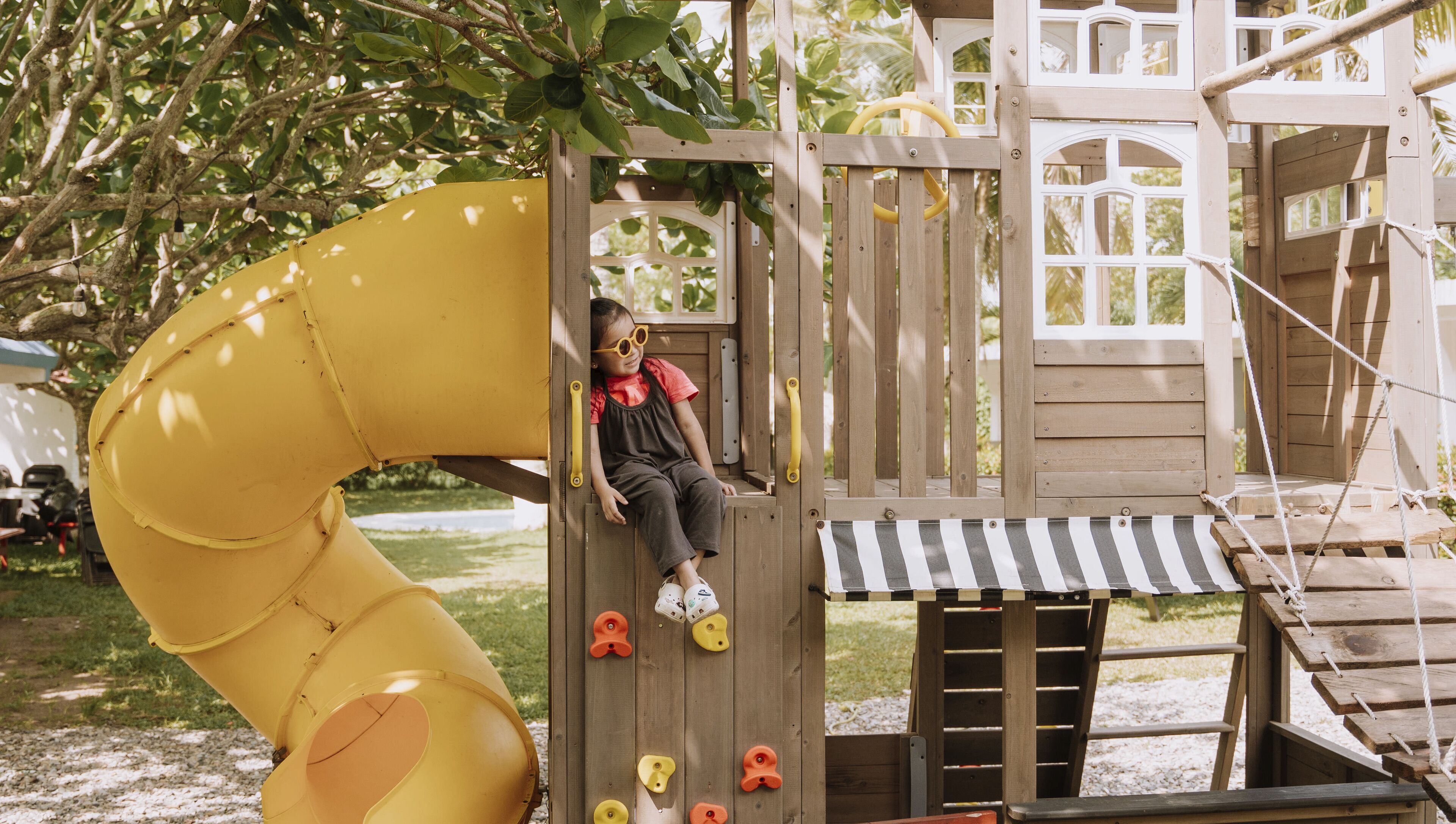A wooden play structure with a yellow slide and climbing holds.