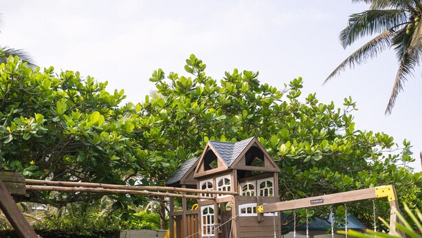 A wooden playhouse with a rope bridge and slide, surrounded by greenery and a clear sky. - Hotel Bungalows Marbella Costa Esmeralda (Tecolutla)