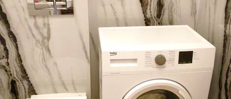 A bathroom with a marble wall, a washing machine, and a toilet.