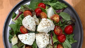 Een bord met salade, groene bladeren, kerstomaatjes en kaas.