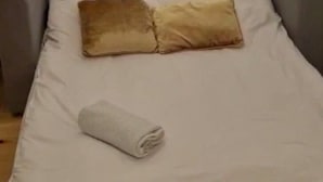 Een bed met twee kussens en een opgerolde handdoek.