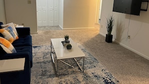 A living room with a blue sofa, a white coffee table, and a TV mounted on the wall.