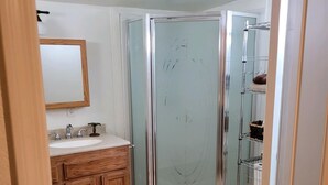 Een badkamer met een houten wastafelmeubel, een douchecabine van glas en een betegelde vloer.