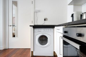 Una cocina compacta con lavadora y secadora integradas, una encimera pequeña y una pared blanca.
