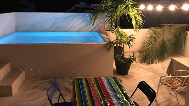 Ein Pool mit Wasserspiel, umgeben von Stühlen und einem Tisch, im Hintergrund eine Palme und Lichterketten.