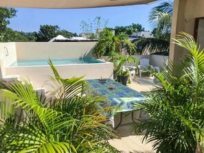 A rooftop pool with a table and chairs, surrounded by lush greenery.