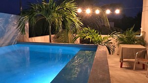 Ein Swimmingpool mit klar blauem Wasser, umgeben von Palmen und einem Tisch mit Stühlen.