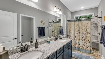 Une salle de bain moderne avec deux lavabos, un grand miroir et une douche agrémentée de rideaux à motifs floraux.