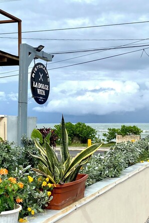 Une enseigne de restaurant avec vue sur la mer et des plantes en pot.