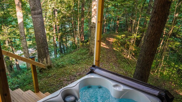 A hot tub in a forested area with wooden deck and natural surroundings. - Creek View, Covered Decks & Private Hot Tub, Woods, Peaceful, Wildlife! (Chillicothe)