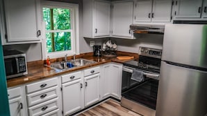 A modern kitchen with white cabinets, stainless steel appliances, a wooden countertop, and a window with a view of greenery. - Creek View, Covered Decks & Private Hot Tub, Woods, Peaceful, Wildlife! (Chillicothe)