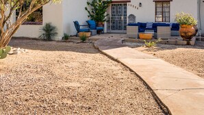 A building with a white exterior, a patio area with outdoor furniture, and a gravel driveway. - Midtown home with Pool Spa, fire pit, close to U of A, Restaurants, & Shopping (Tucson)