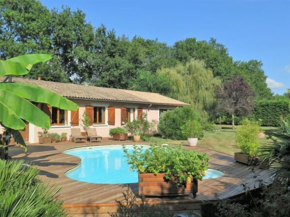 A house with a swimming pool, surrounded by lush greenery and trees.