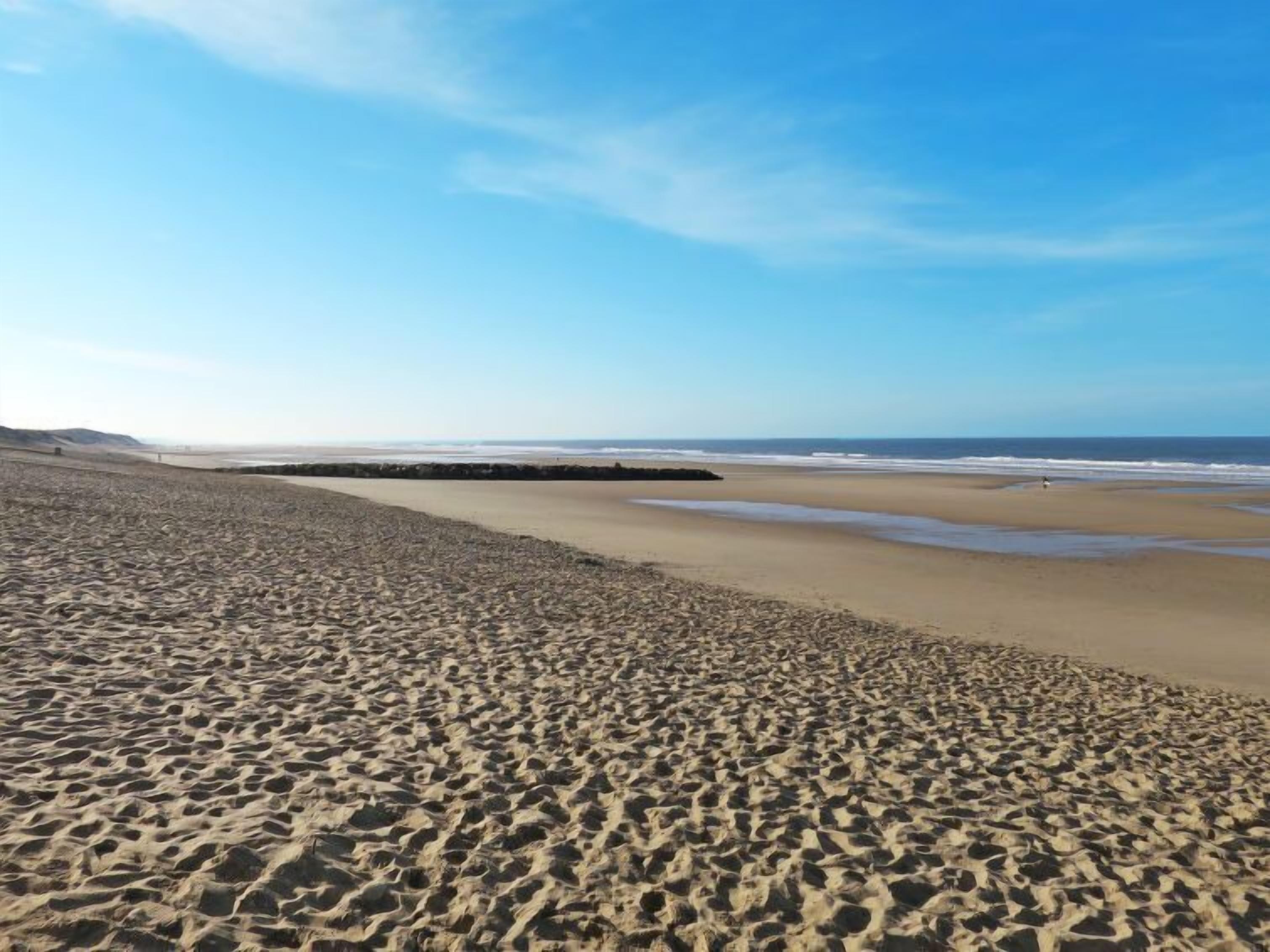 A wide sandy beach with gentle waves and a clear sky.