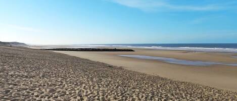 A wide sandy beach with gentle waves and a clear sky.